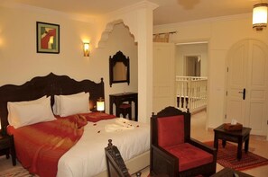 A hotel room with a large bed, a chair, a nightstand, a bedside table, a mirror, and a door leading to a balcony. - Hotel Riad Benatar (Essaouira)