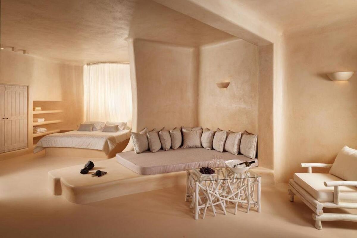 A spacious room with a large bed, a seating area with cushions, a glass coffee table, and a white armchair.