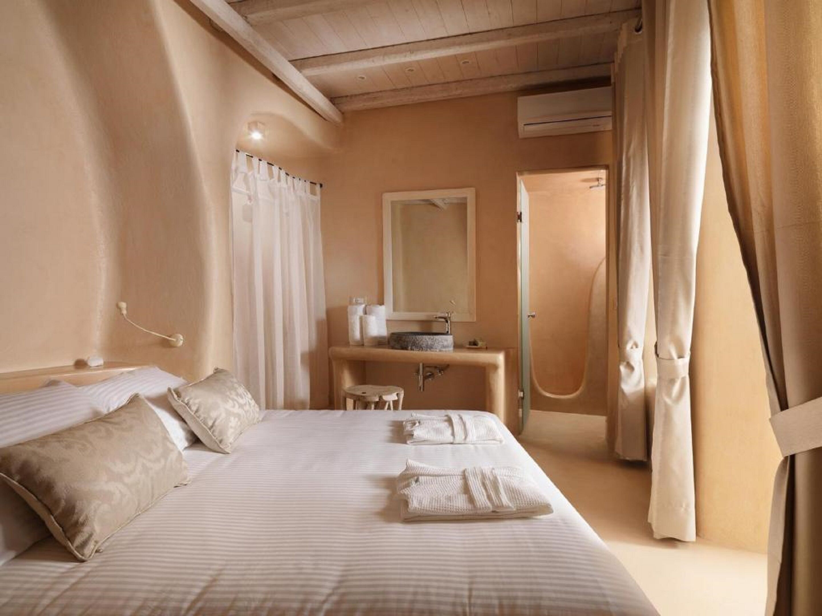A hotel room with a large bed, a bedside table with a mirror, and a bathroom visible through an open door.