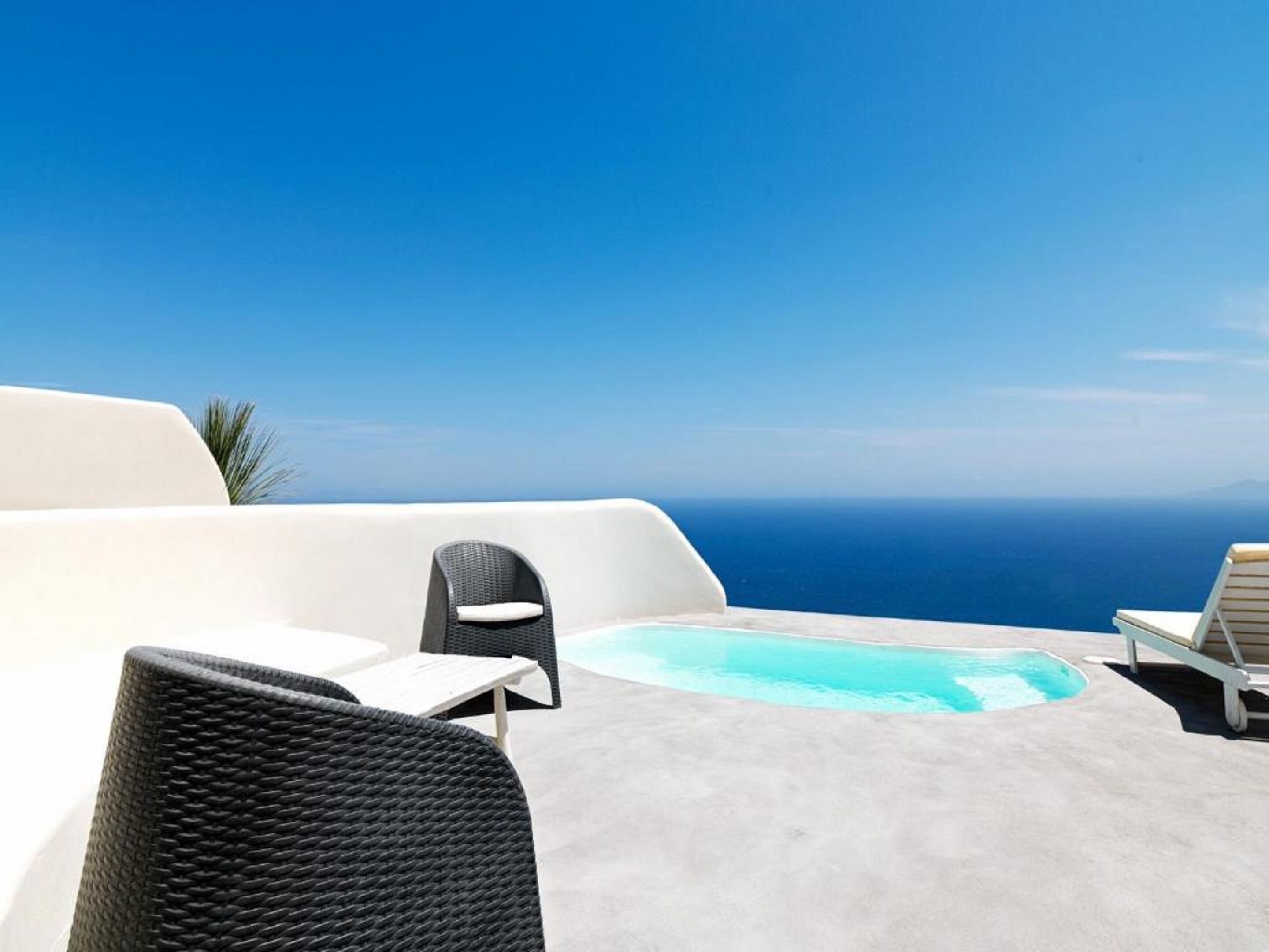 A poolside area with lounge chairs and a small pool, overlooking a clear blue sky and the sea.