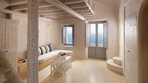 Una habitación amplia con un banco incorporado, una pequeña mesa y vista al mar por una ventana.