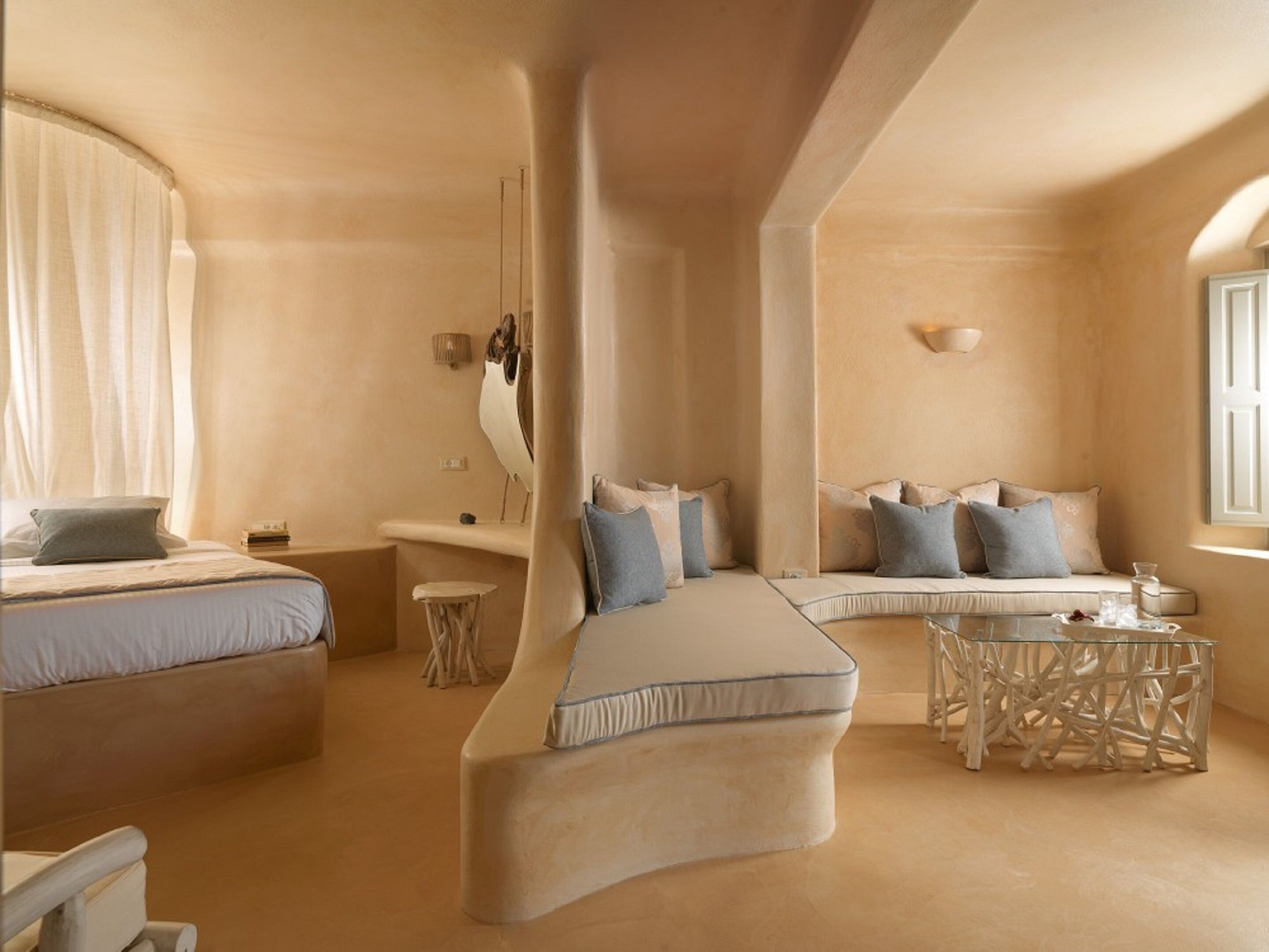 A modern bedroom with a curved bed, a sofa bed, a small round table, and a large window.