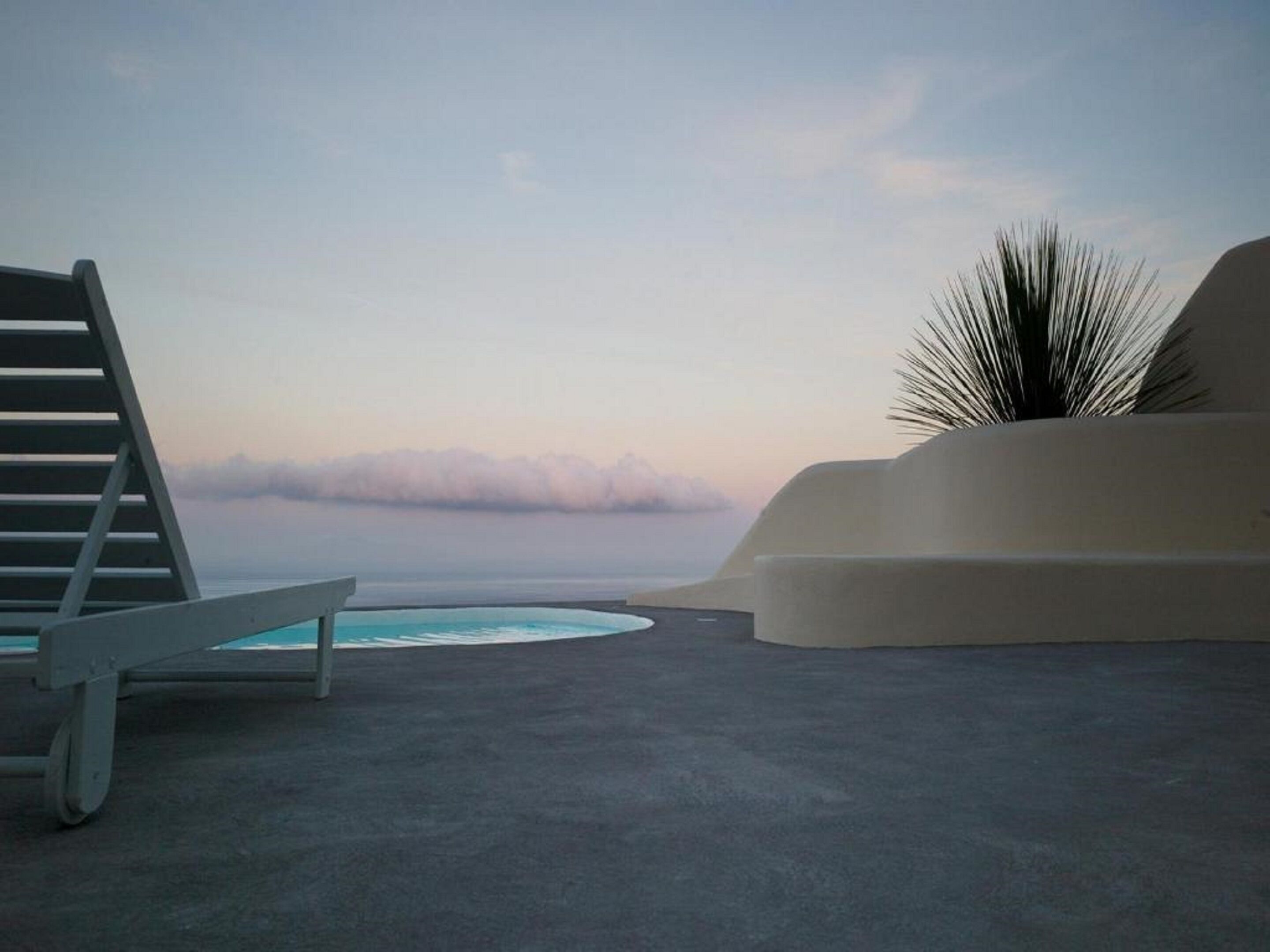 A modern outdoor seating area with a pool, a lounge chair, and a palm plant.