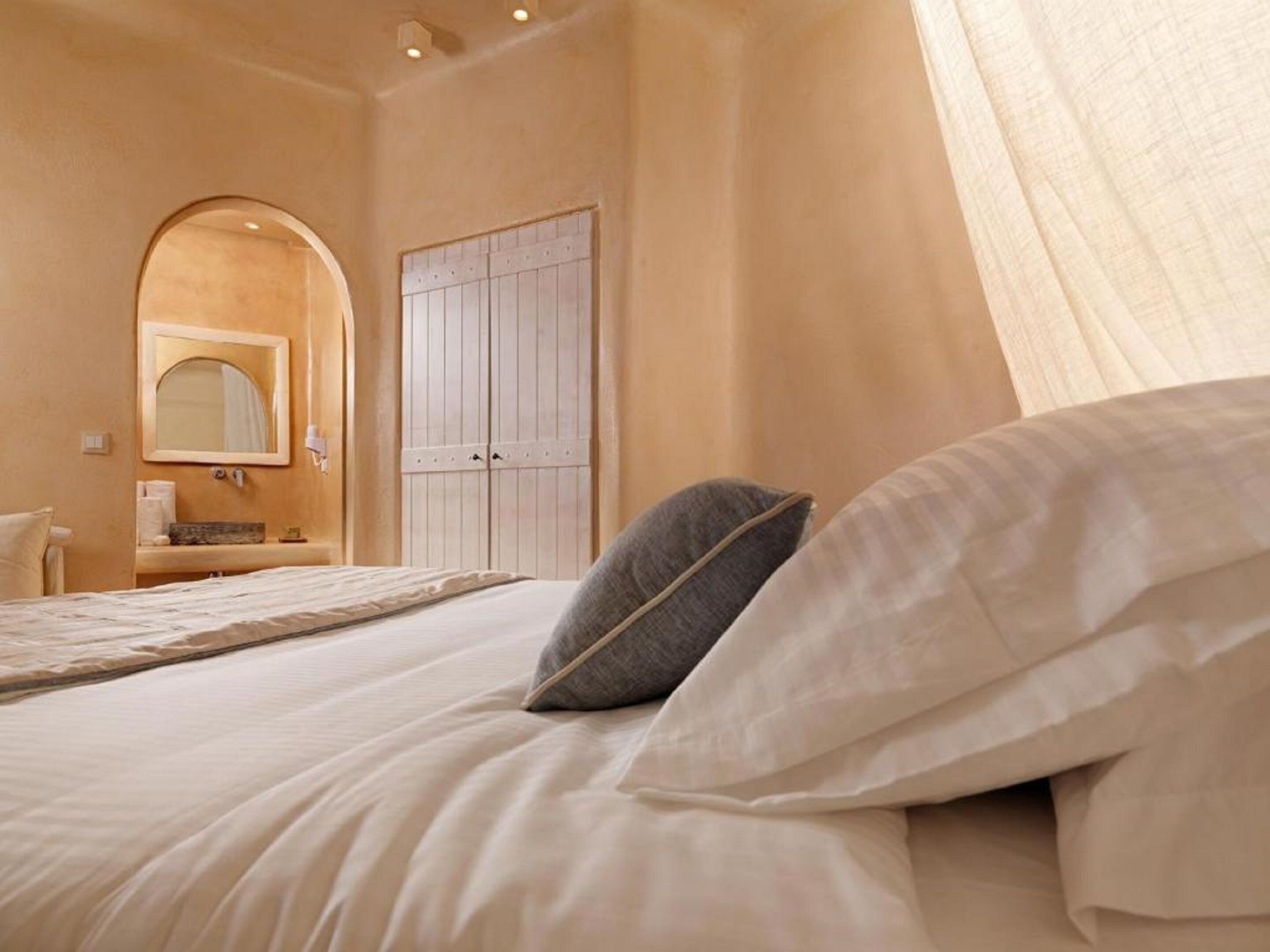 A bedroom with a bed, pillows, a mirror, a wardrobe, and a bathroom area.