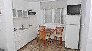 Cocina compacta con una mesa, sillas, refrigerador, microondas y pileta.