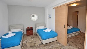 Habitación de hotel con dos camas, un armario de madera, una cómoda pequeña de madera, un espejo redondo en la pared y suelo de baldosas.