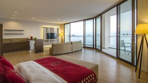 Een moderne hotelkamer met een groot bed, een zithoek, een televisie, een balkon met uitzicht op zee en een eethoek.