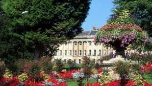 A large, classical building with a symmetrical facade, surrounded by a well-maintained garden with various flowering plants and a central fountain. - Brocks Guest House (Bath)