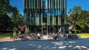 A modern building with a glass facade, outdoor seating area with tables and chairs, and a well-maintained garden. - Brocks Guest House (Bath)