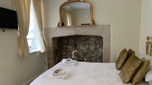A hotel room with a stone fireplace, a bed with white linens, and a gold-framed mirror above the fireplace. - Brocks Guest House (Bath)