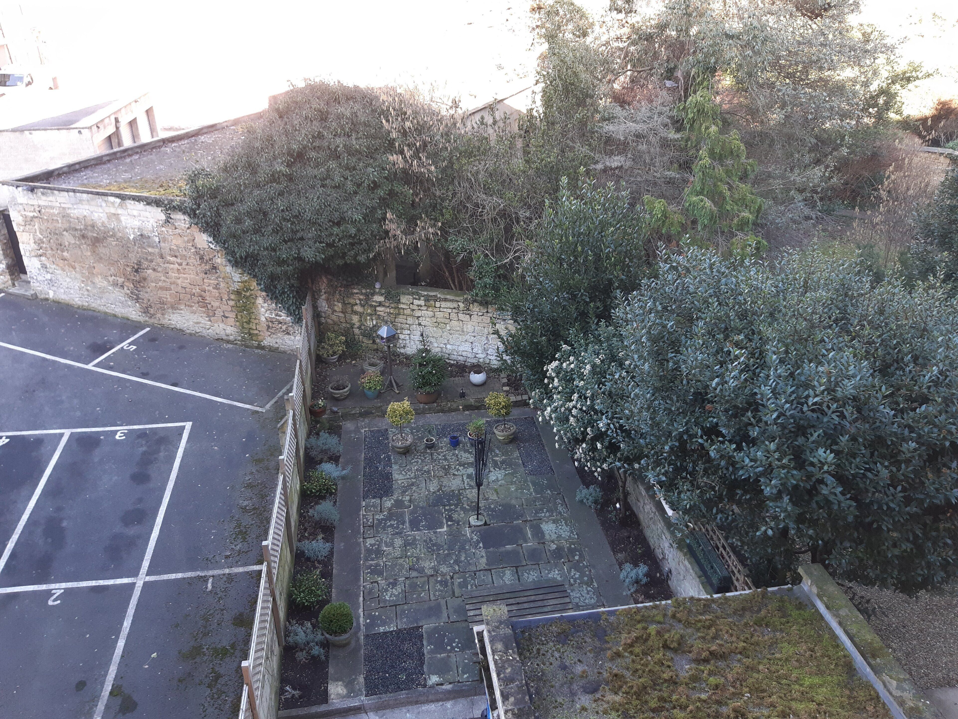 Un patio con suelo empedrado, muros de piedra y diversas macetas con plantas.