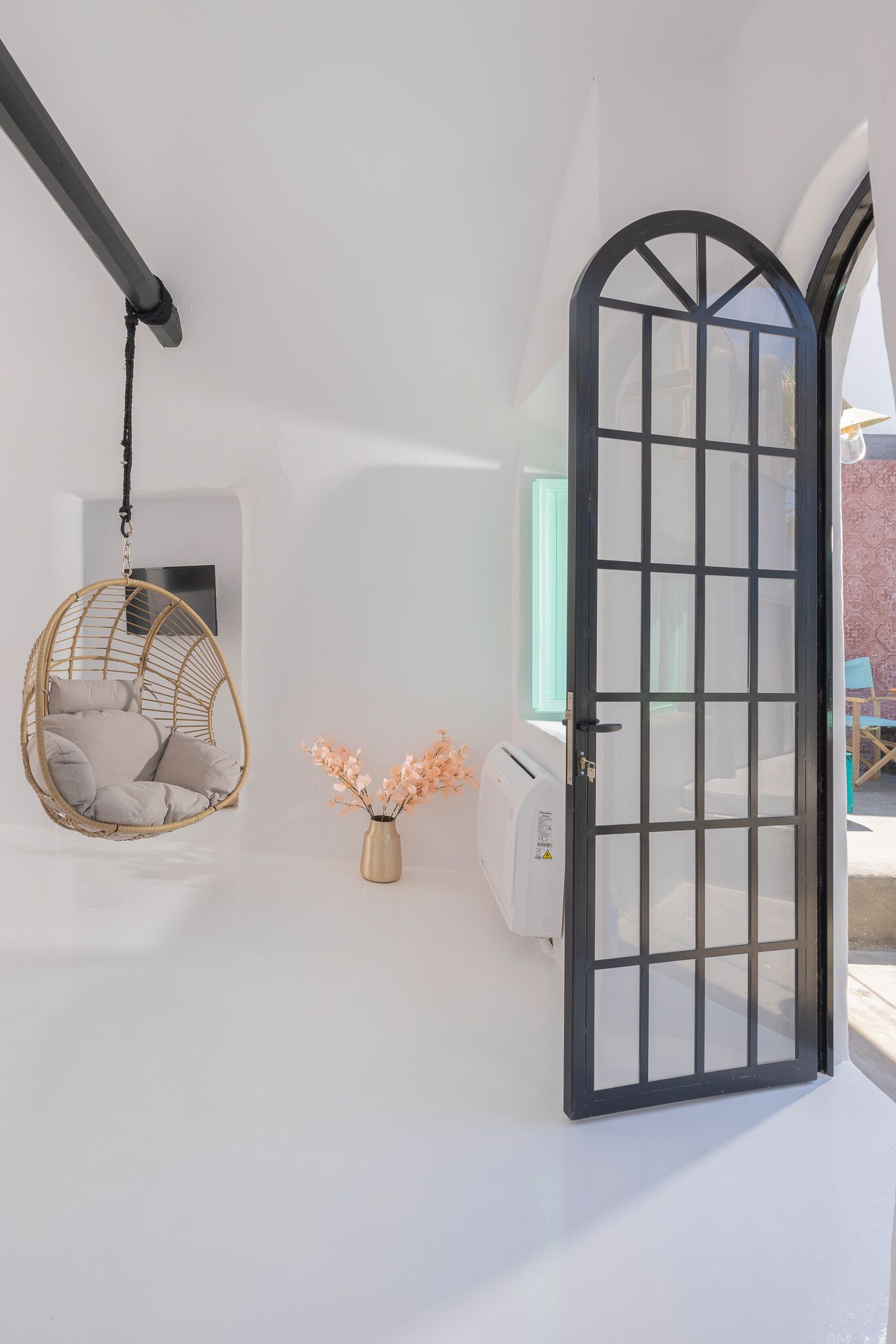 A room with a black-framed door, a hanging chair with cushions, and a vase with flowers.