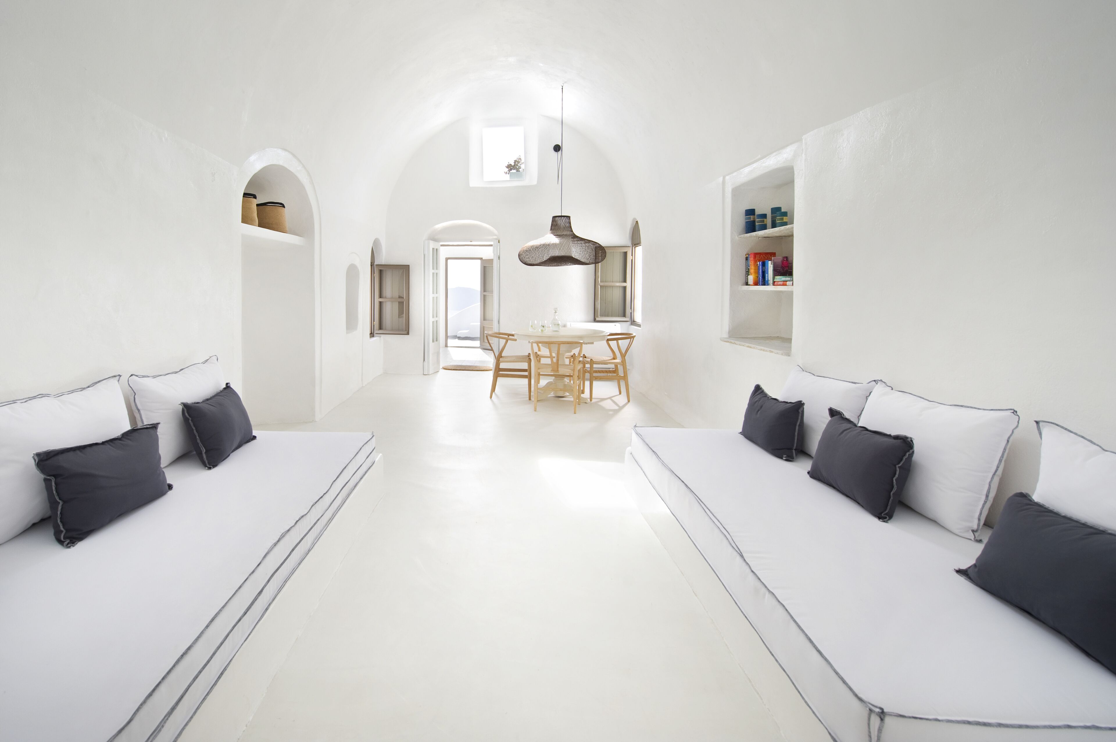 A spacious room with white walls, a central dining table, and two white sofas with black cushions.