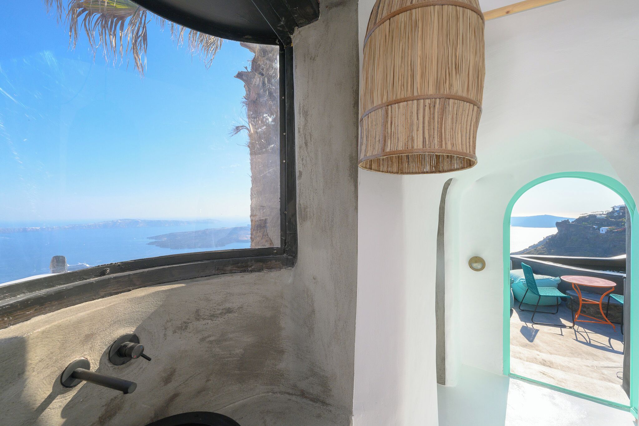 Een kamer met uitzicht op zee, een rieten lamp en een glazen deur naar een terras.