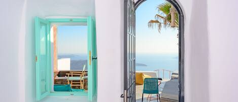 A room with a view of the sea, a balcony with a chair, and a window with a teal frame.