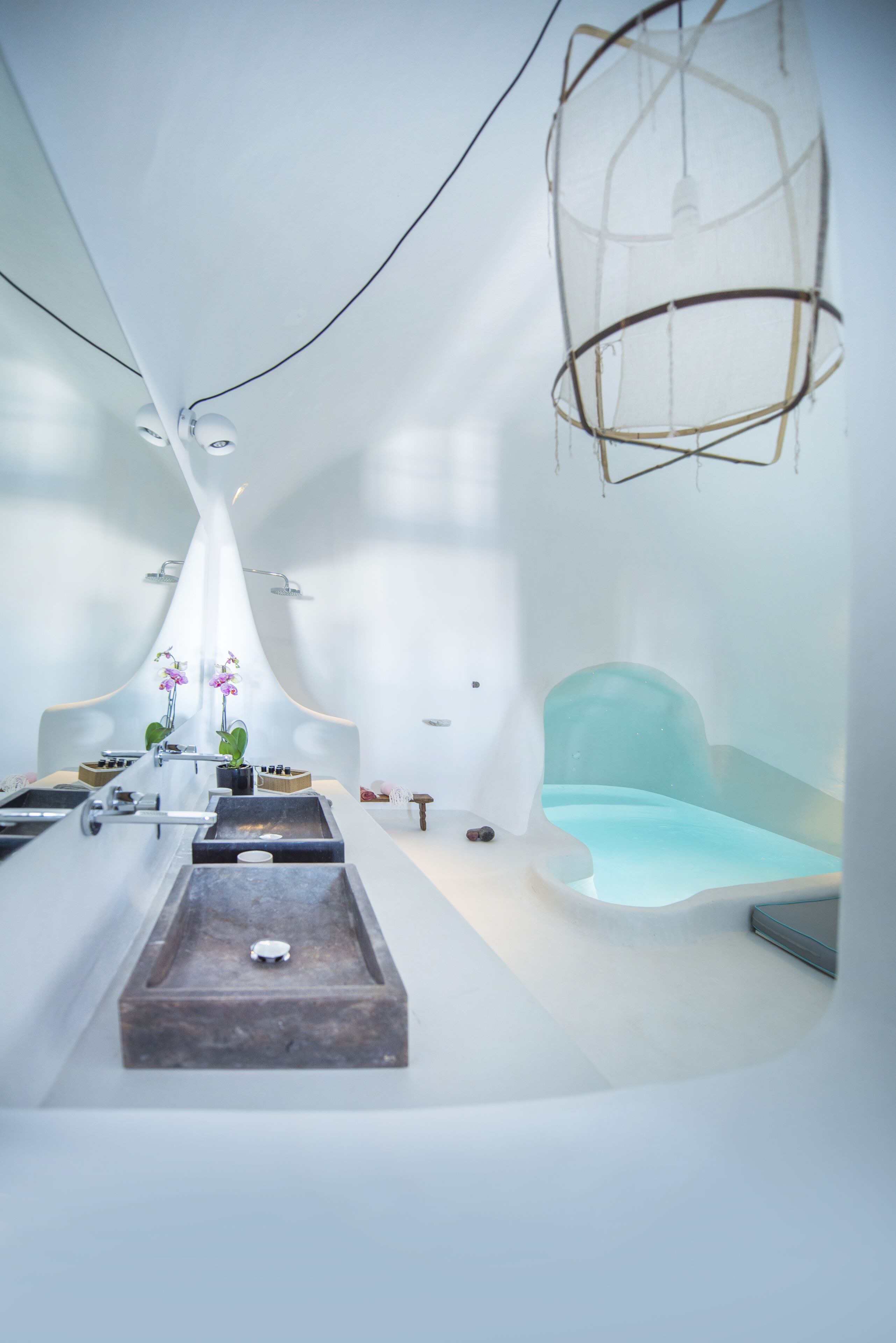 A modern spa room with a minimalist design, featuring a large bathtub, a small seating area, and a decorative hanging light fixture.