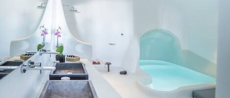 A modern spa room with a minimalist design, featuring a large bathtub, a small seating area, and a decorative hanging light fixture.