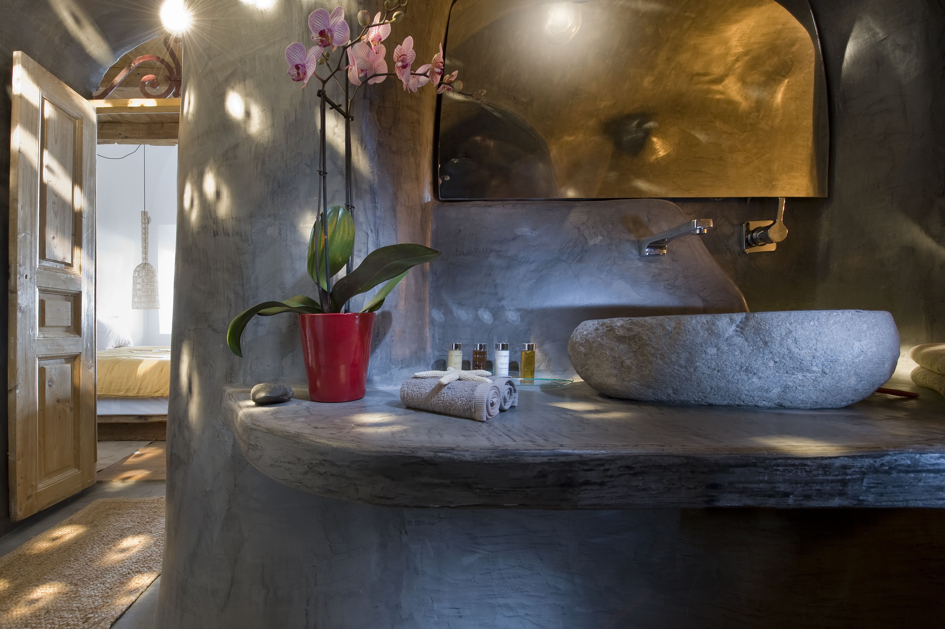 A bathroom with a stone basin, a red pot with a plant, and toiletries on a shelf.