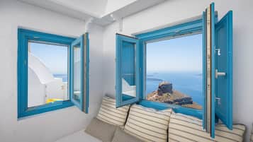 Habitación con vista al mar, con pared blanca, ventanas con marco azul y cojines a rayas.