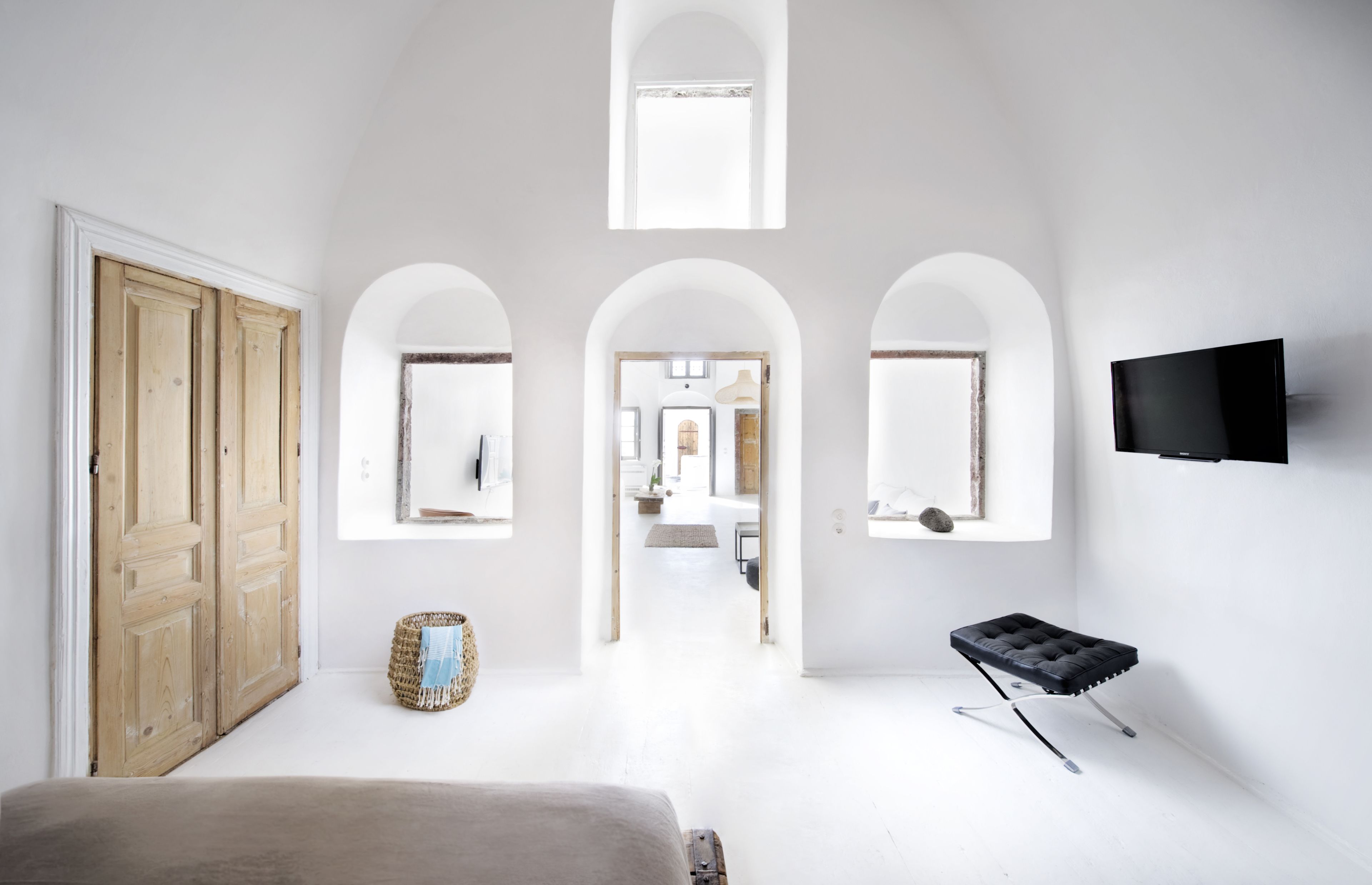 A room with a bed, a television, and a view of a hallway with an arched ceiling.