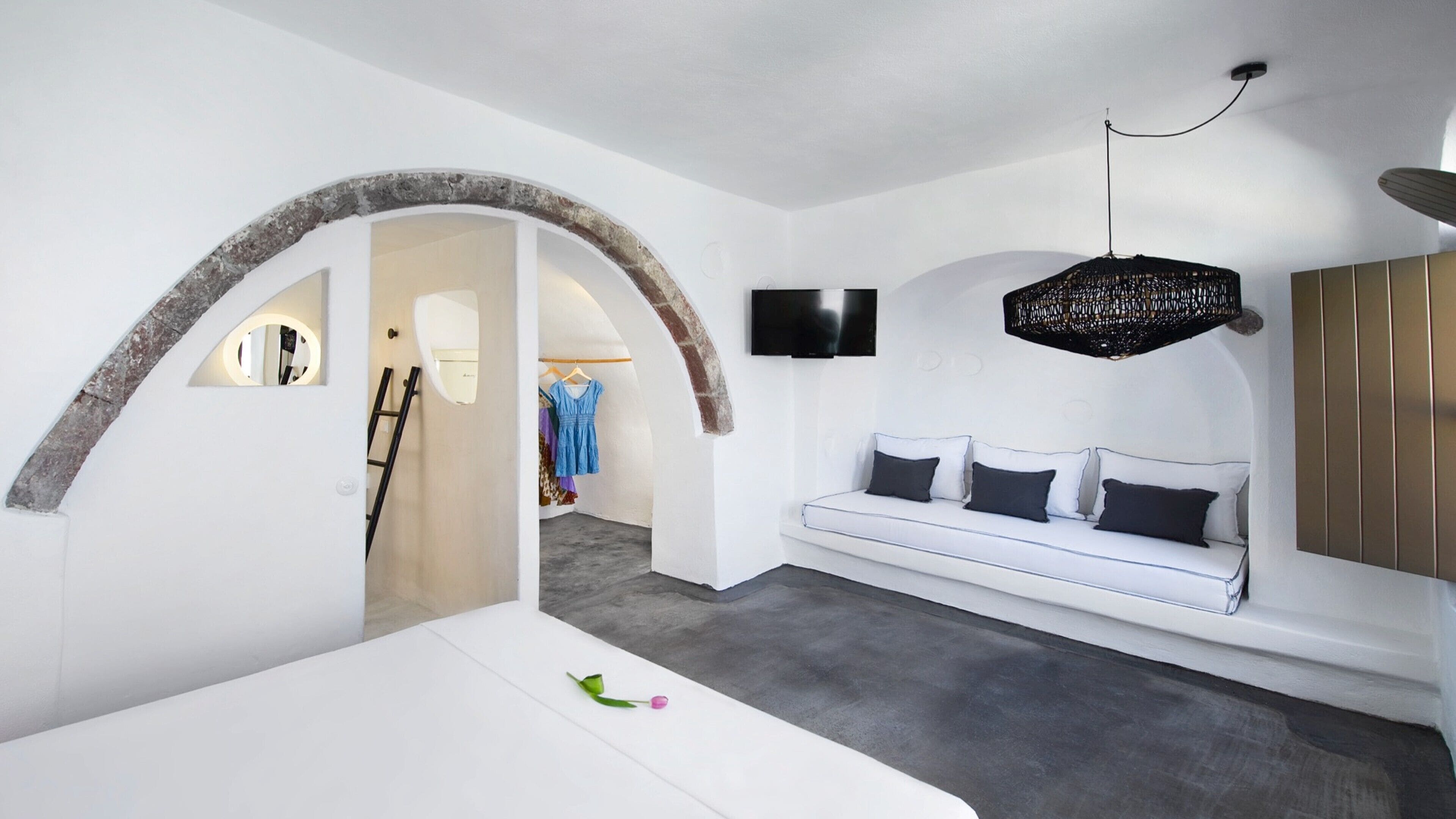 Un interior moderno con un sofá blanco, una lámpara de araña negra colgante y una pared blanca con un televisor montado.