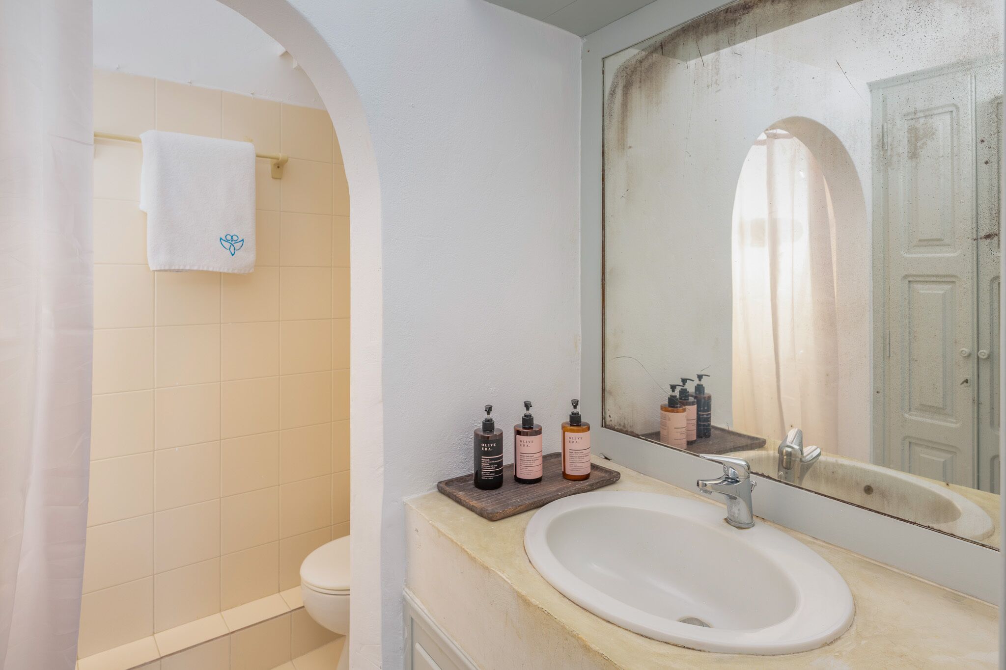 A bathroom with a white sink, a mirror, and toiletries on a wooden tray.