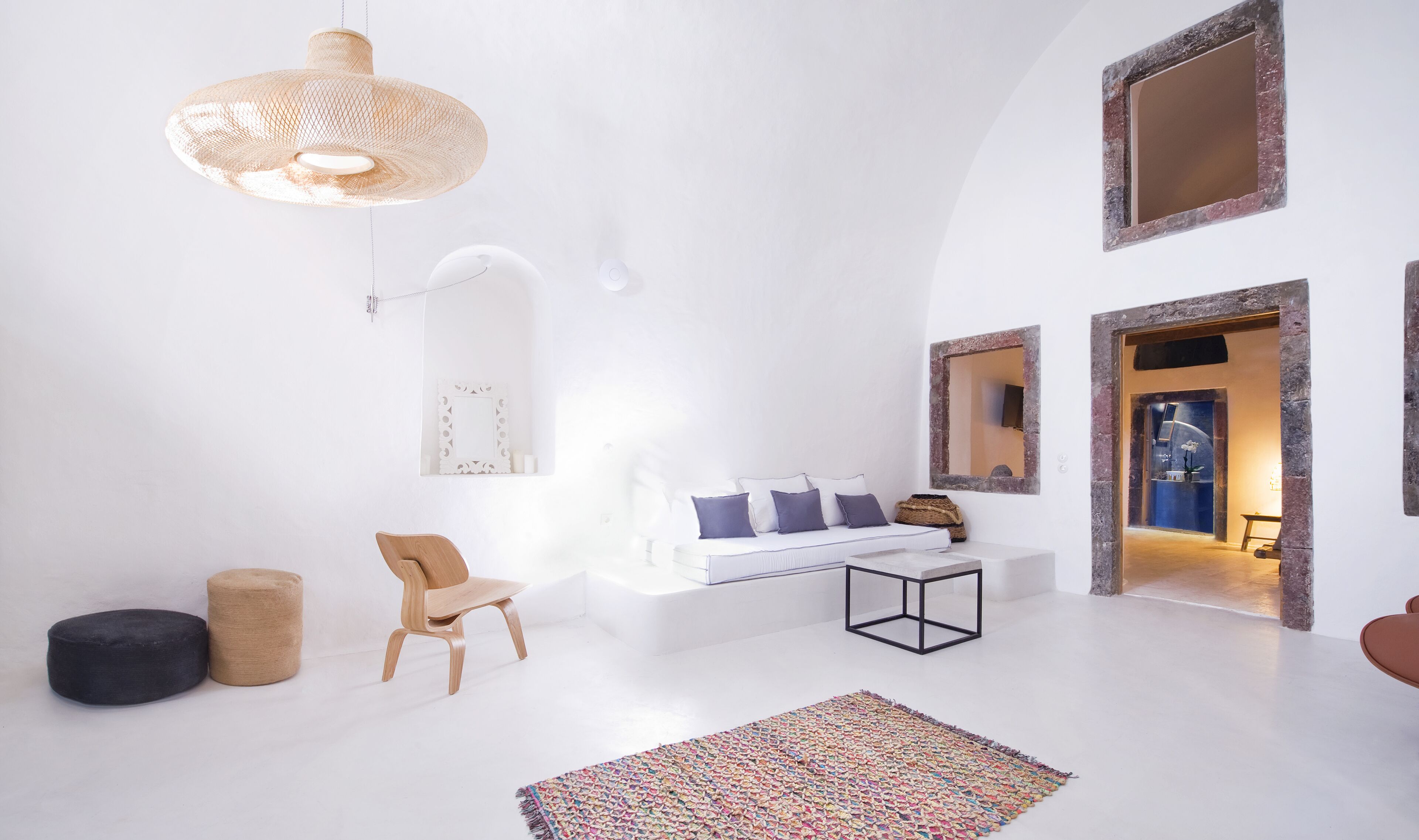 A minimalist room with a white sofa, a wooden chair, a small table, and a colorful rug.