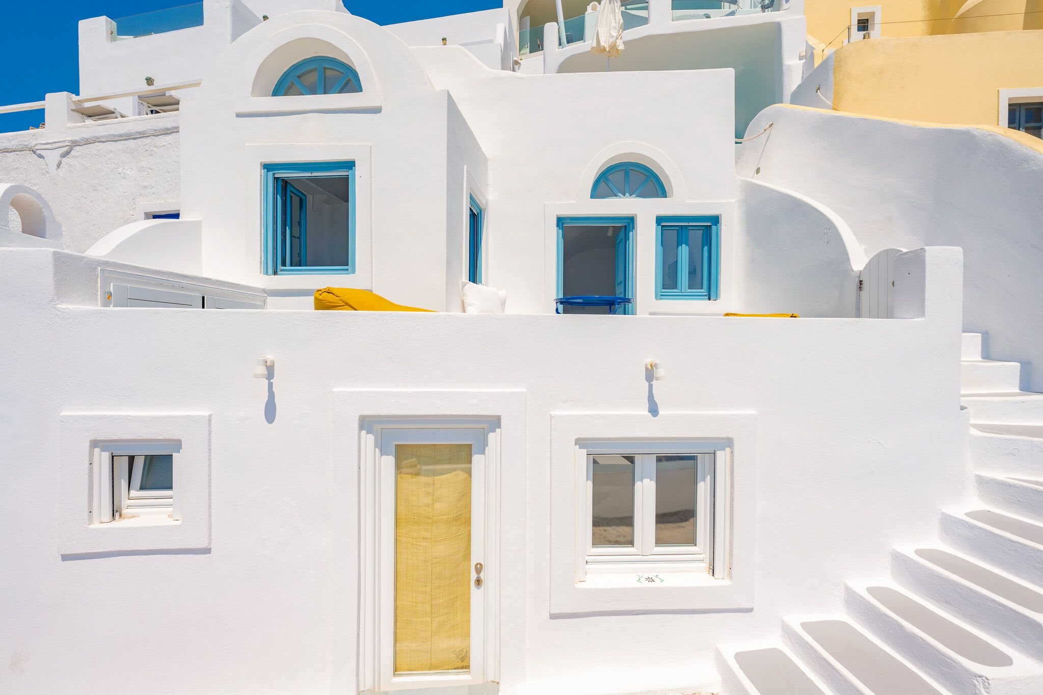A white building with blue windows and doors, white steps, and a yellow towel hanging on a railing.