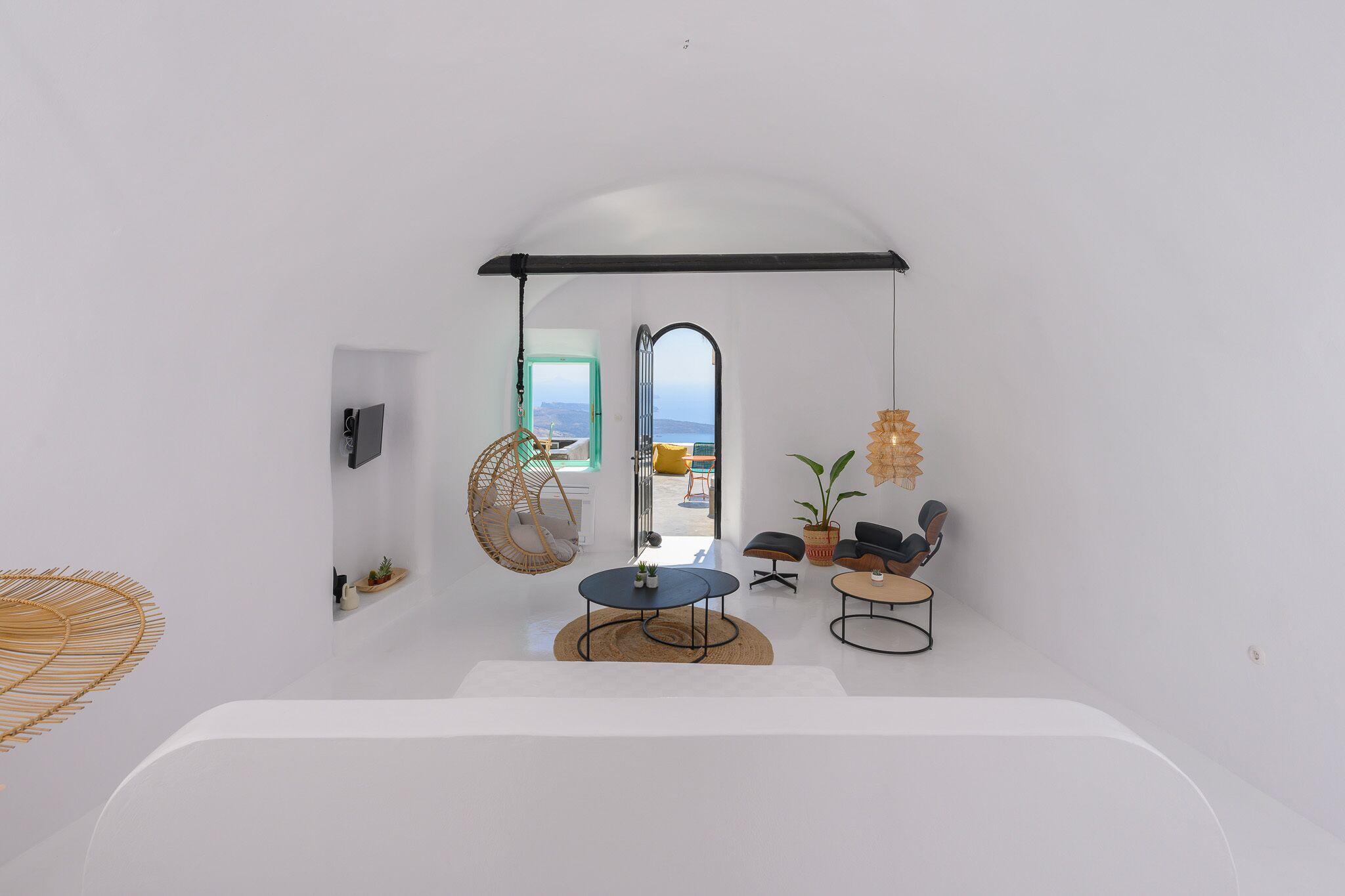 A minimalist room with a large window, a hanging chair, a round table, and a sofa.