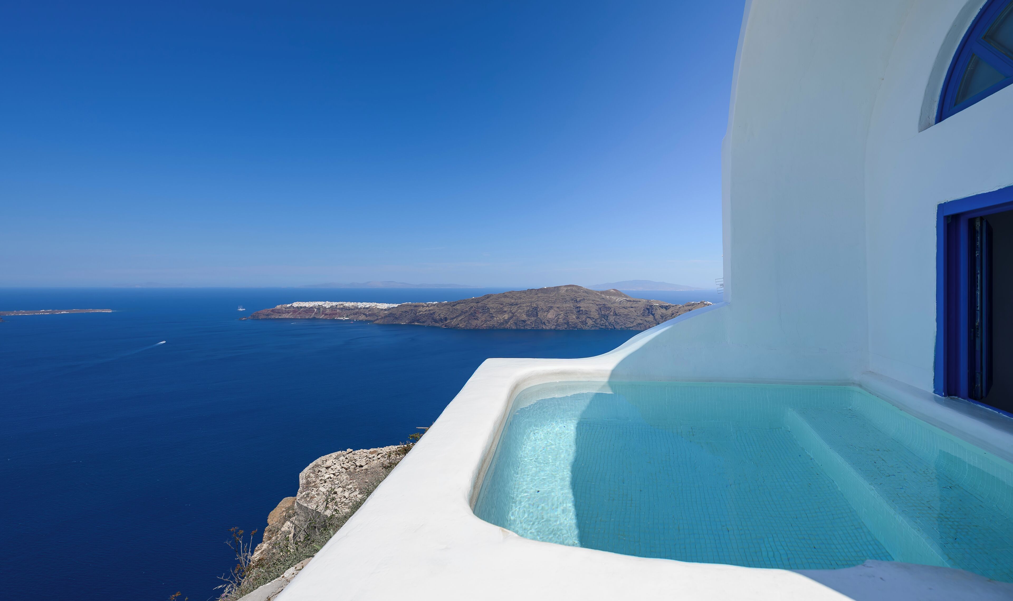 A white building with a pool overlooking the sea and a distant island.