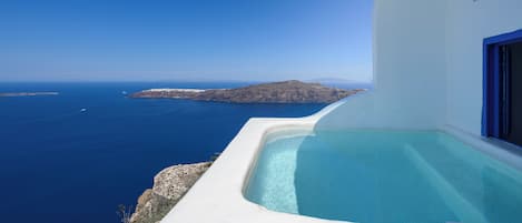 A white building with a pool overlooking the sea and a distant island.