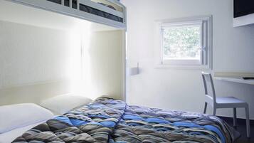 Uma cama de solteiro com edredom listrado, uma escrivaninha com cadeira e uma janela com vista para árvores.