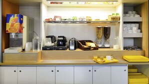 A well-organized breakfast bar with a variety of food and drink options, including a juice dispenser, coffee maker, toaster, and baskets of bread. - hotelF1 Saint Etienne La Grand Croix (La Grand-Croix)