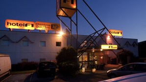 A hotel with multiple signs indicating 'hotelFT' and 'hotelFT.com'. There are cars parked in front, and the building has a modern design with a flat roof. - hotelF1 Saint Etienne La Grand Croix (La Grand-Croix)