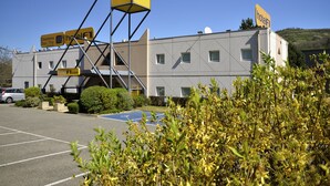 A hotel with a prominent yellow sign, a parking lot, and some greenery in the foreground. - hotelF1 Saint Etienne La Grand Croix (La Grand-Croix)