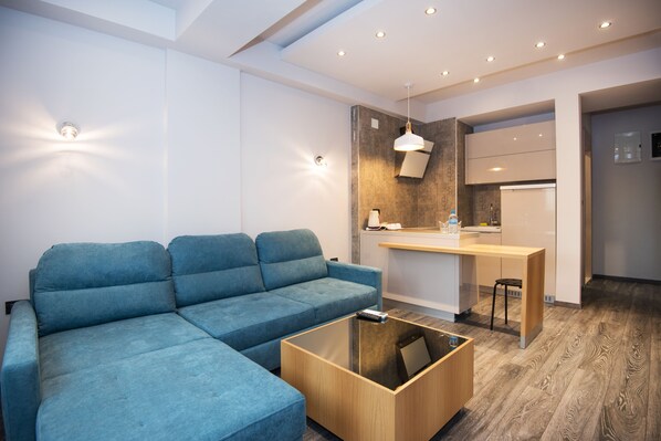 En moderne stue med en modulsofa, et glasbord og et køkkenområde med bordplade og hængende lampe.