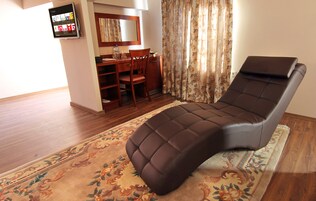 A massage chair in a room with a wooden floor, a desk with a chair, and a large mirror.