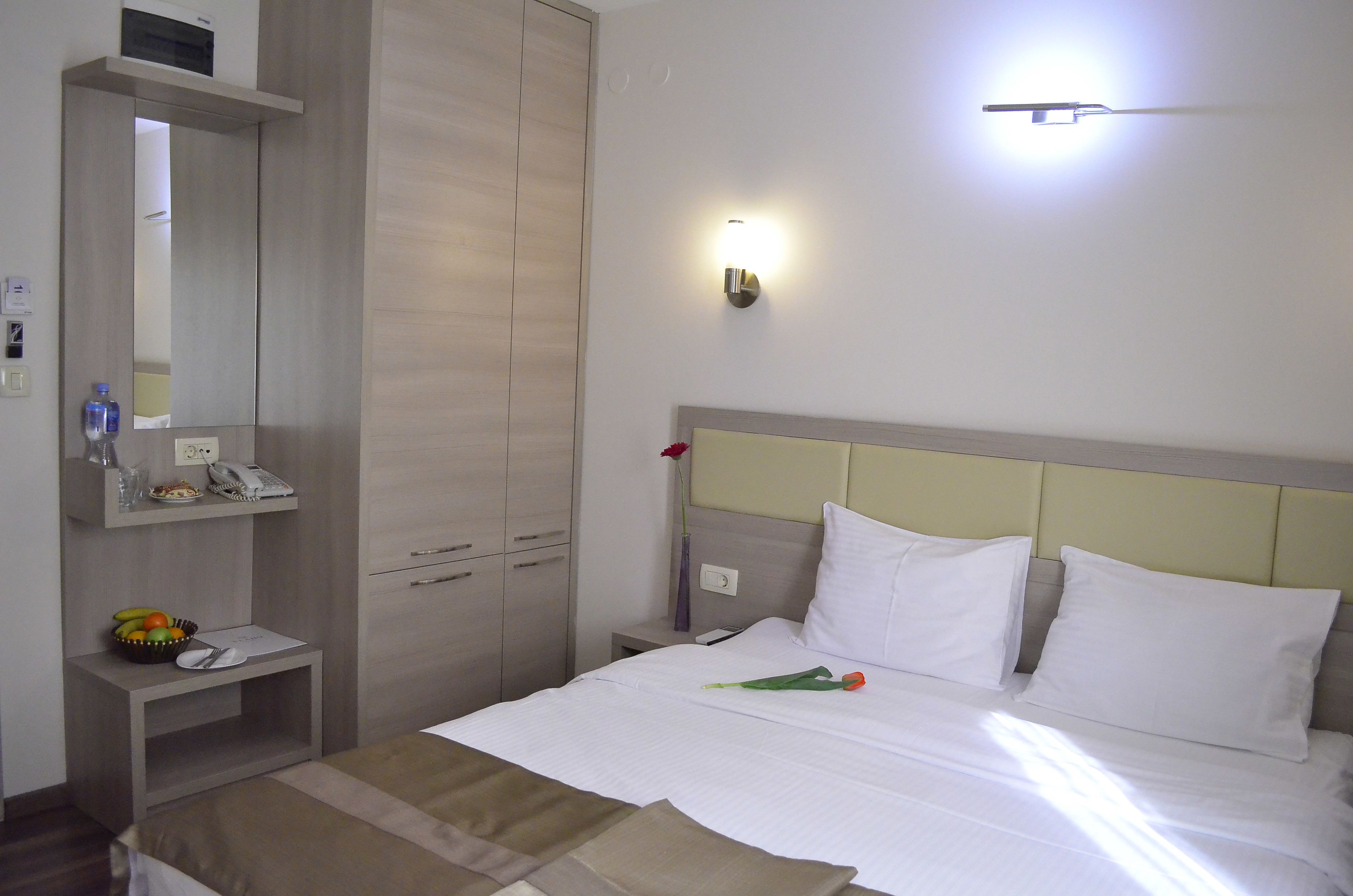 Et hotelværelse med en seng, et natbord, et spejl, et skab og en lampe på væggen.