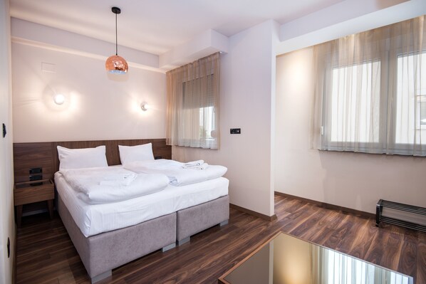 A modern hotel room with a large bed, wooden flooring, and a large window with sheer curtains.