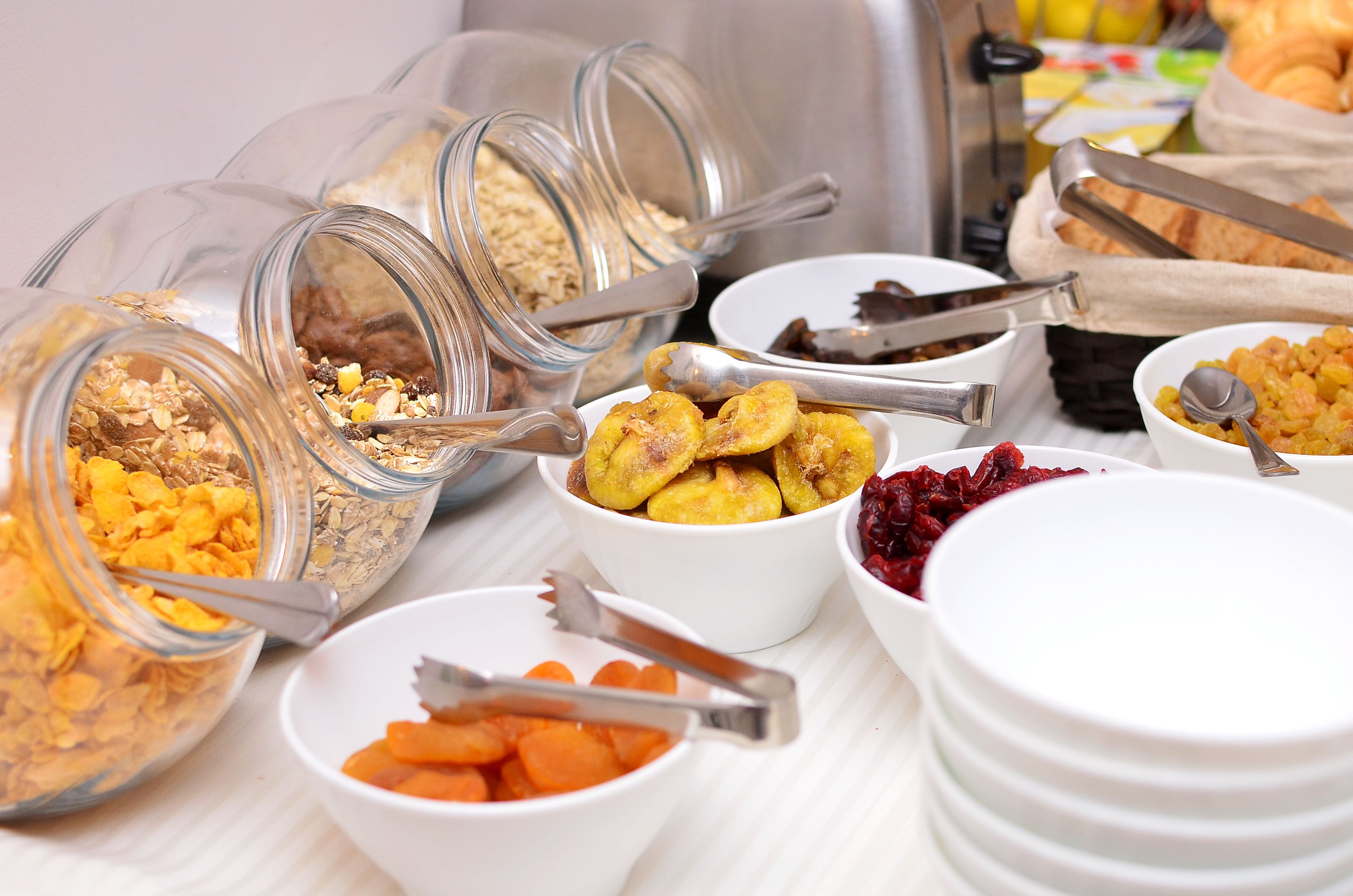 Een buffettafel met diverse soorten eten, zoals ontbijtgranen, bananen, gedroogd fruit en wortels.