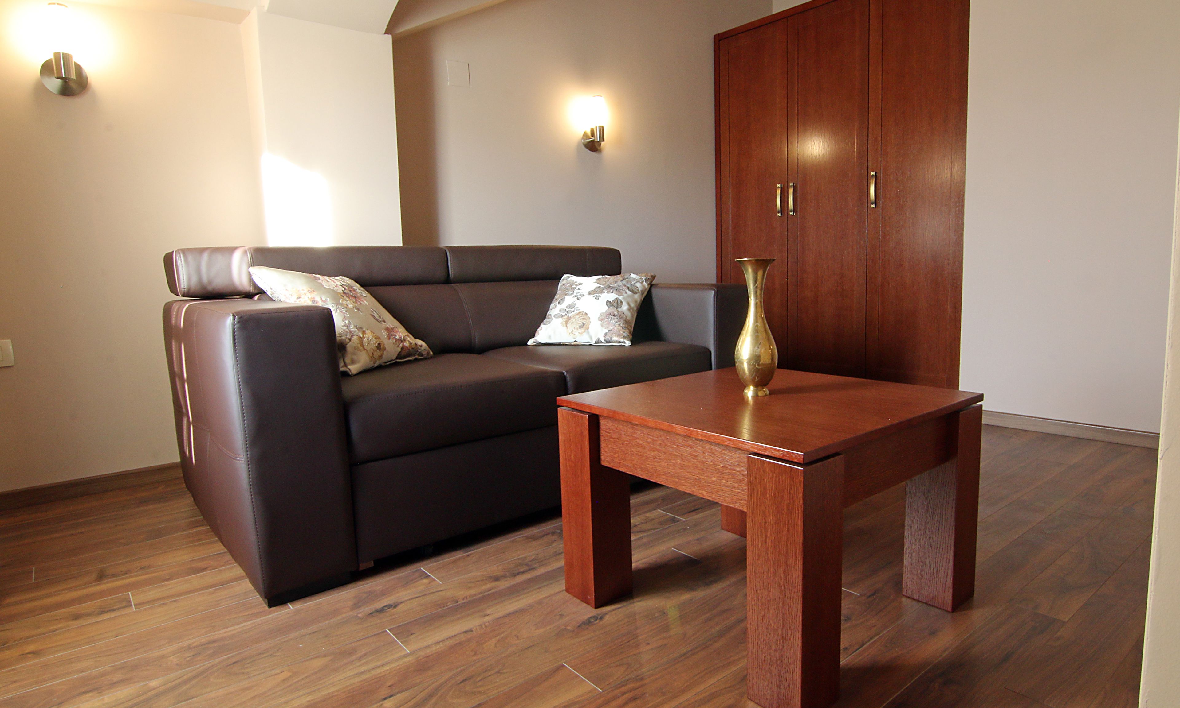 A living room with a brown leather sofa, two decorative pillows, a wooden coffee table, and a wooden cabinet.