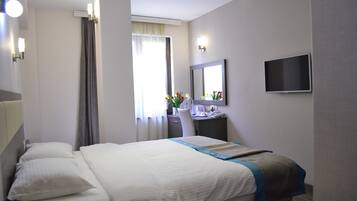 Une chambre d’hôtel comprenant un lit, un bureau avec une chaise, un téléviseur à écran plat et une fenêtre avec des rideaux.