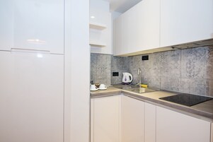 A modern kitchen with white cabinets, a grey tiled backsplash, and a stainless steel sink.