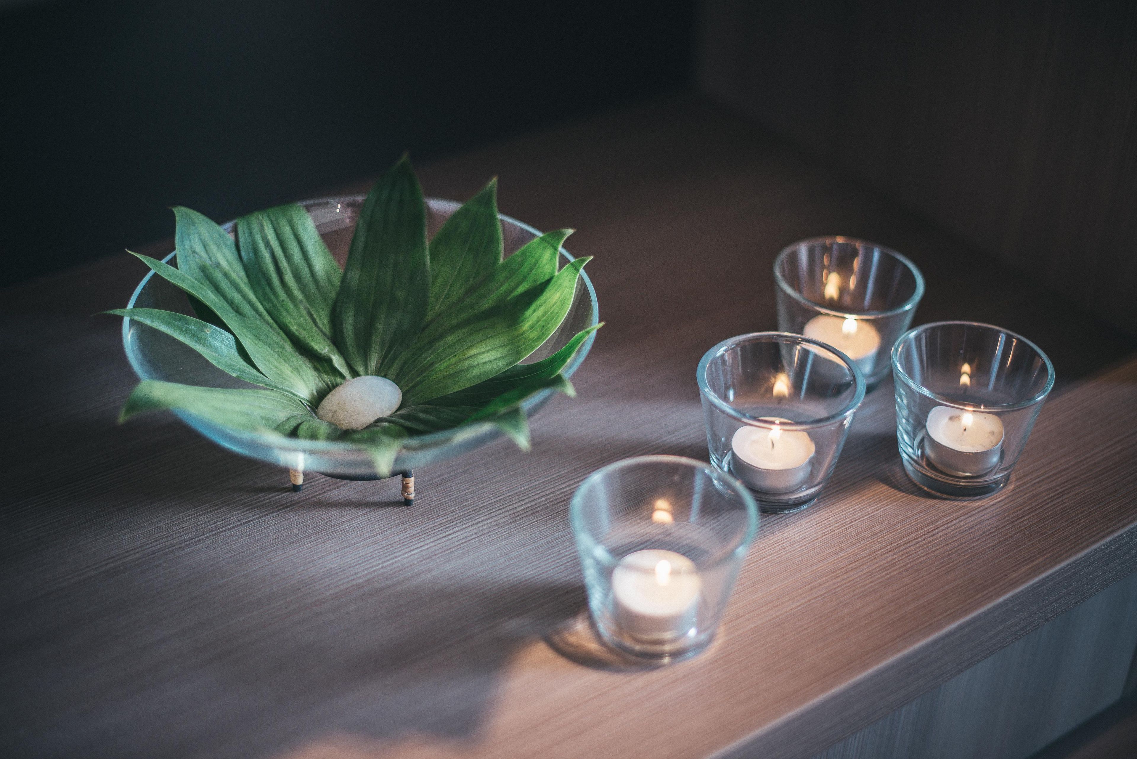 A glass bowl with a plant and a candle on a wooden surface.