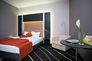 A hotel room with a bed, a chair, a table, and a vase with a flower. - Best Western Plus Lakeside Hotel (Szekesfehervar)