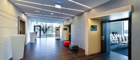 Un moderno vestíbulo de hotel con un largo pasillo, una recepción y una zona de estar con un banco rojo y gris.