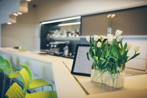 Mostrador de recepción con un jarrón de tulipanes blancos, un menú y una barra de bar al fondo.