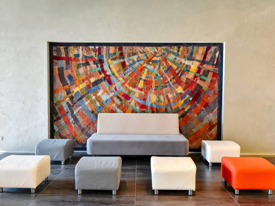 A modern room with a large abstract painting on the wall, a grey sofa, and four ottomans in white and orange.