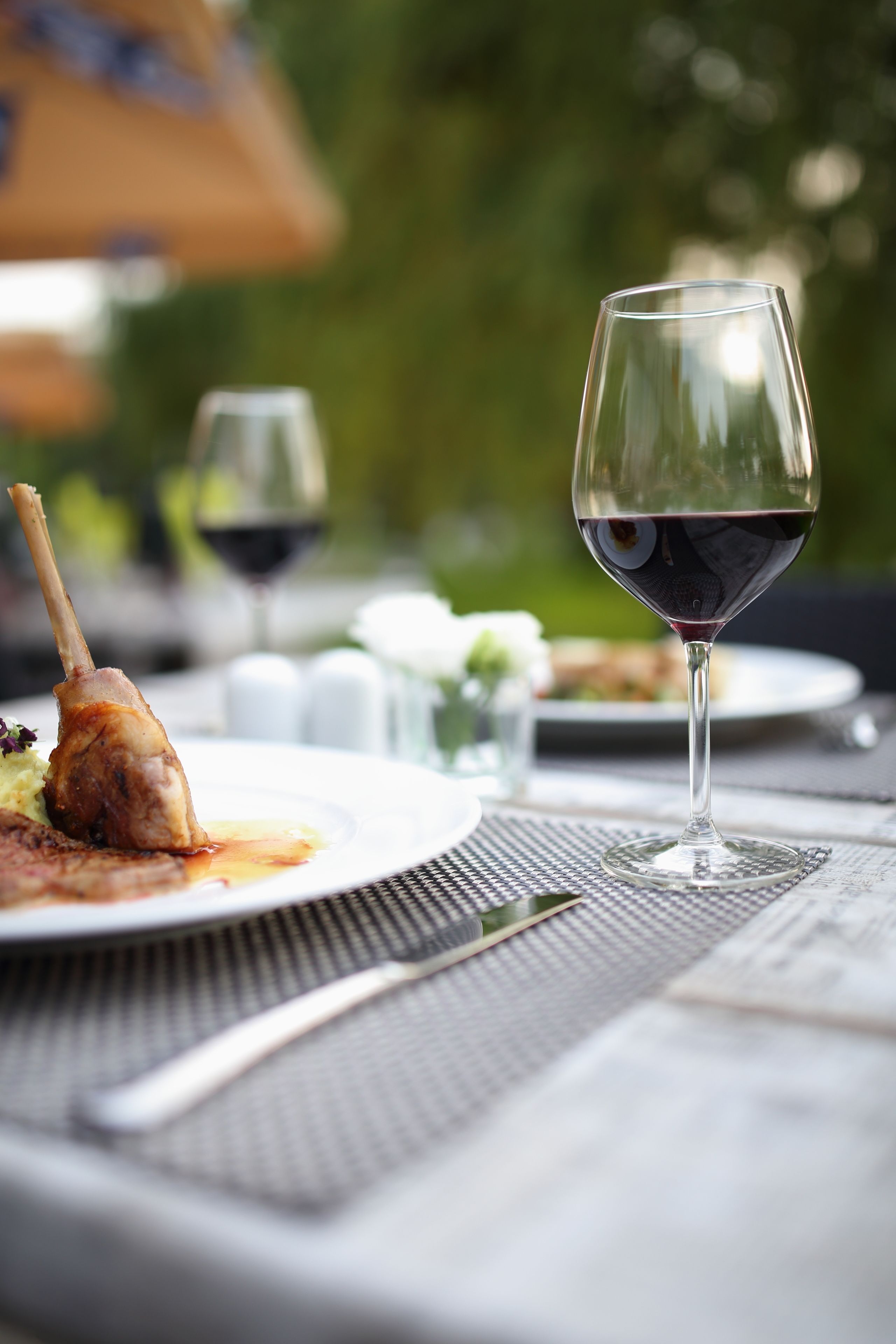 A dining table with a glass of red wine, a plate with food, and a fork.