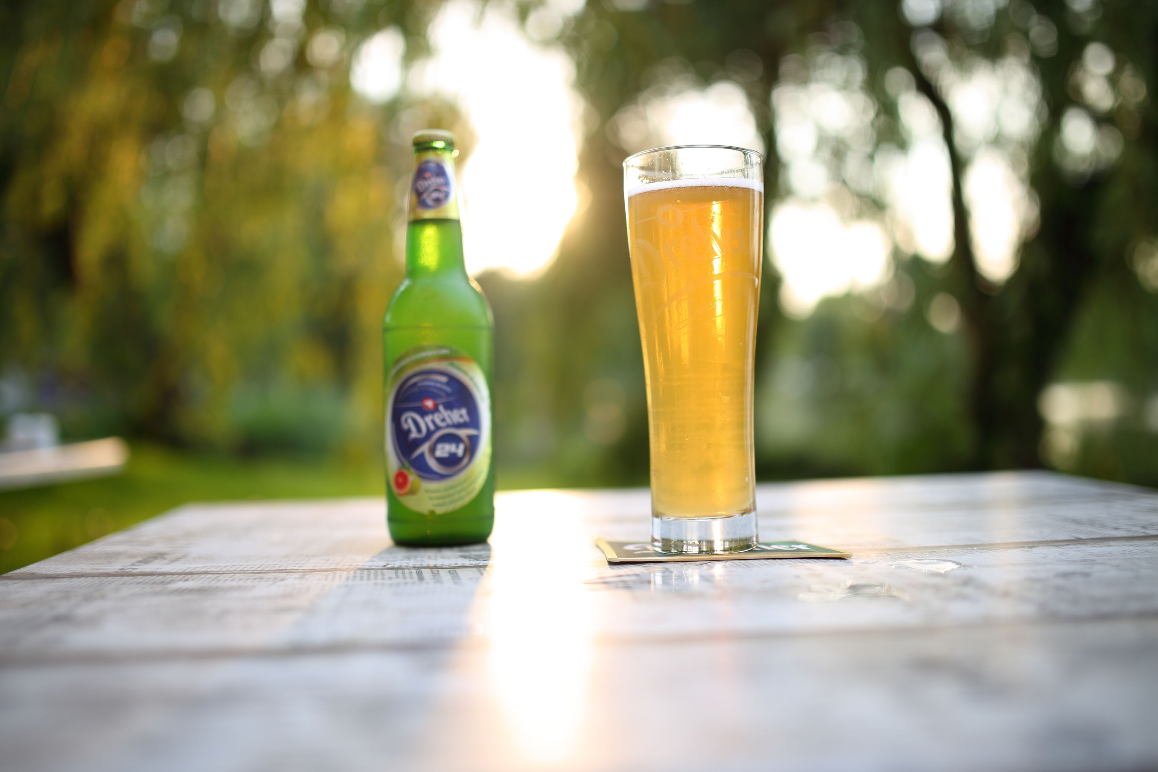 A bottle of beer and a glass on a wooden table outdoors.